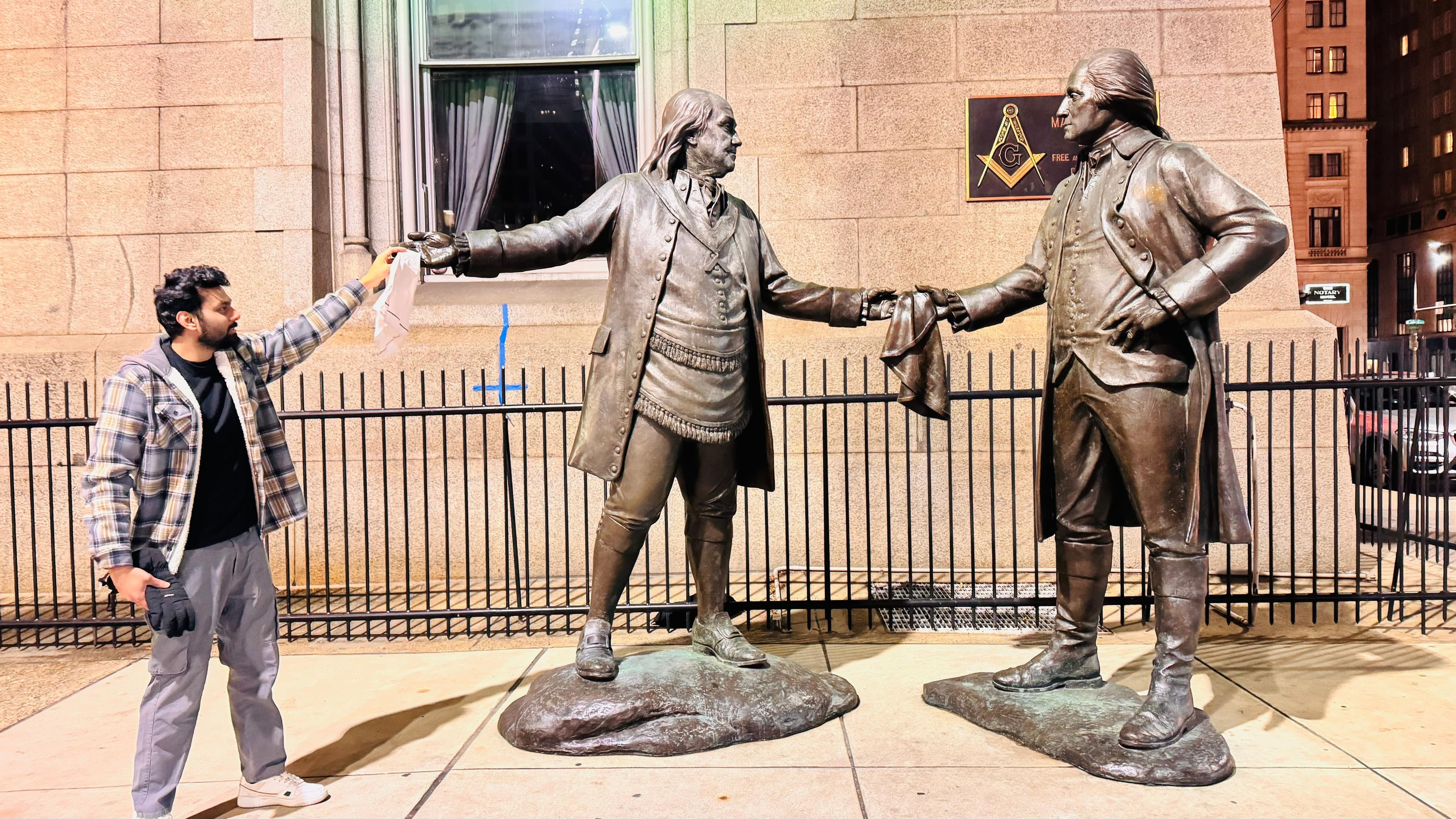 Night photo shaking hands with the Brotherhood bronze statues outside a Philadelphia Masonic temple
