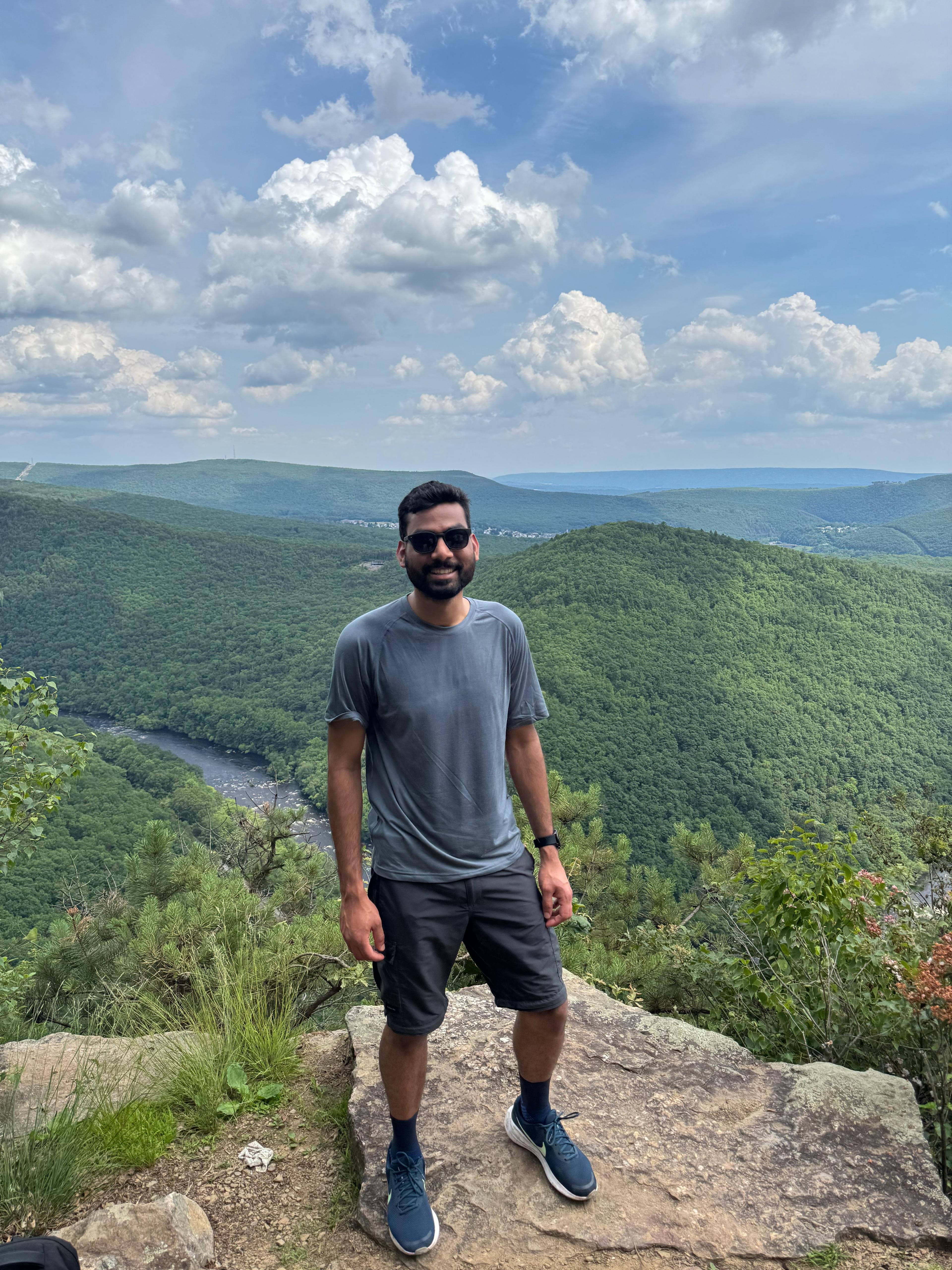 Standing on a rocky overlook above a green river valley under a bright cloudy sky