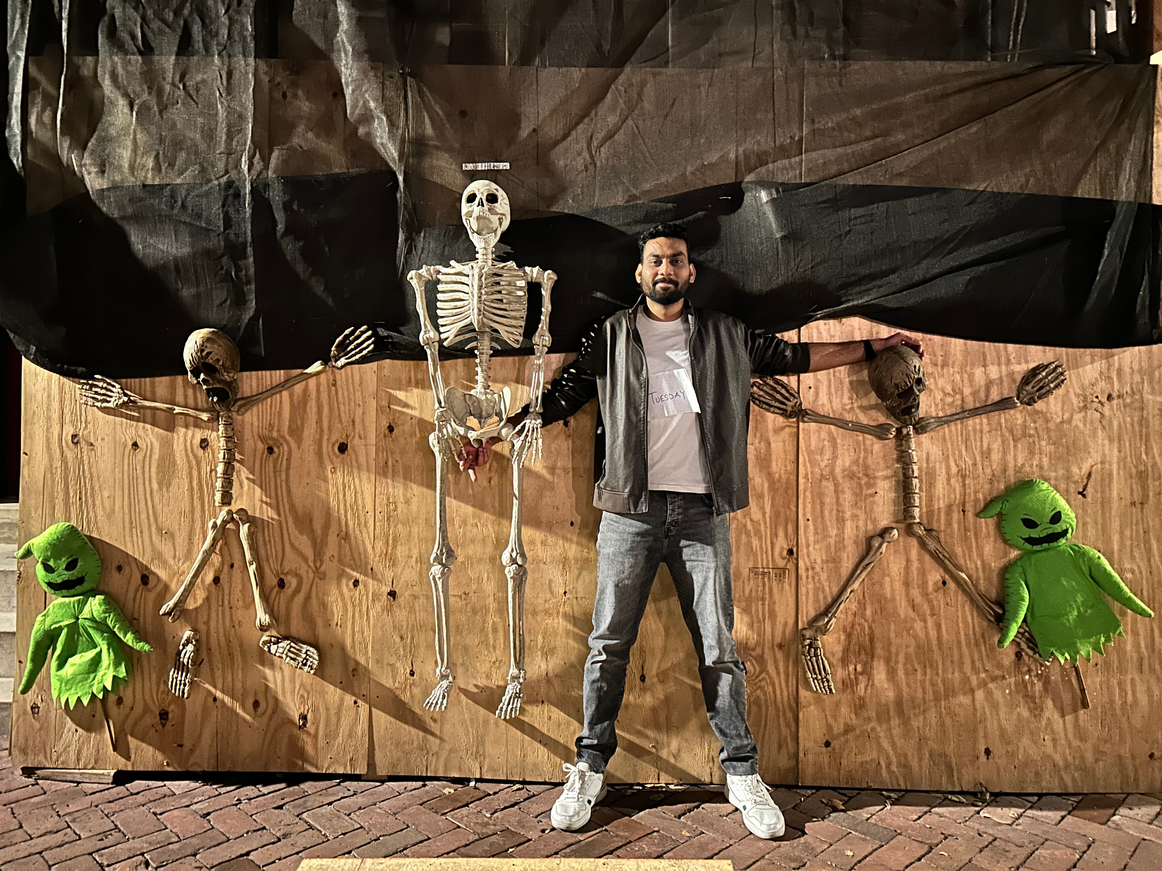 Posing at night in front of Halloween skeleton and Oogie Boogie decorations with a Tuesday name tag